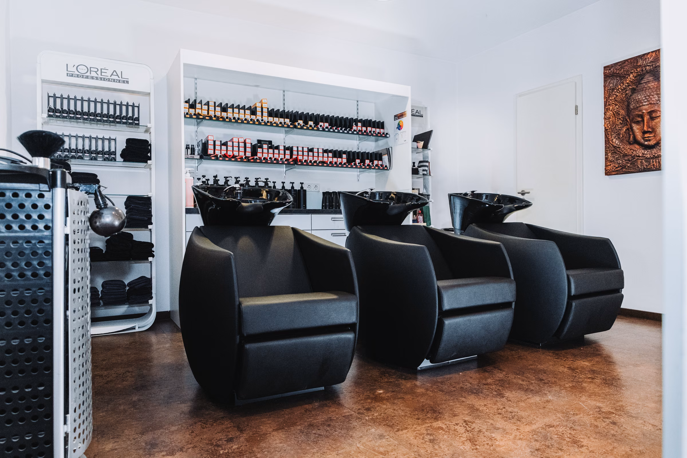 Drei schwarze Waschplätze im Friseursalon Irena, dahinter die Regalwand mit Farben und Pflegeprodukten.