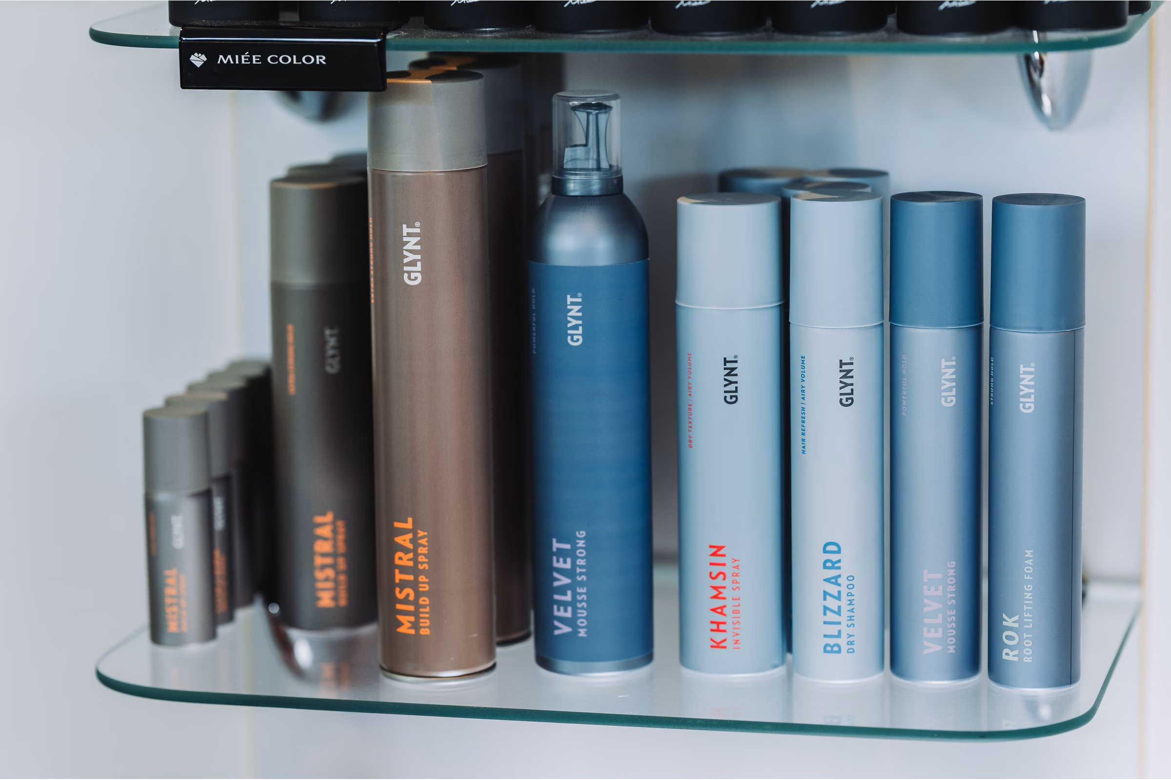 Nahaufnahme einer Produktreihe auf einem Glasregal im Friseursalon Irena, Verpackungen in Rot, Blau und Silber.
